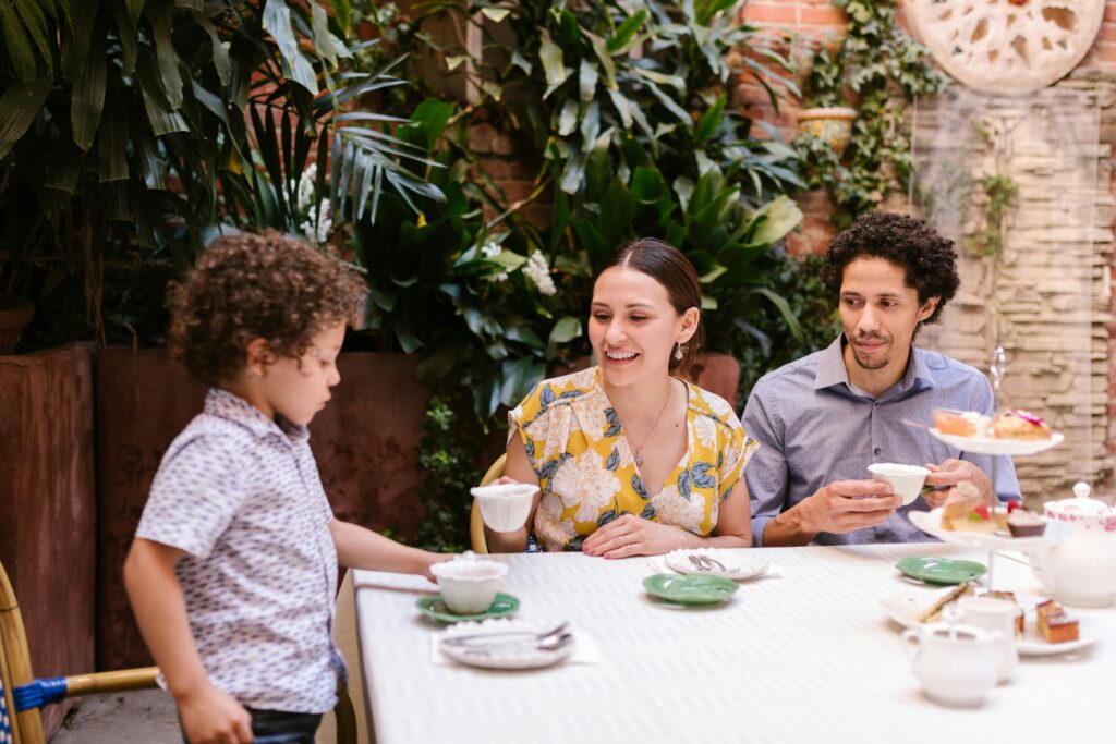 A family having afternoon tea together on their garden table outside with the little boy standing next to the table.