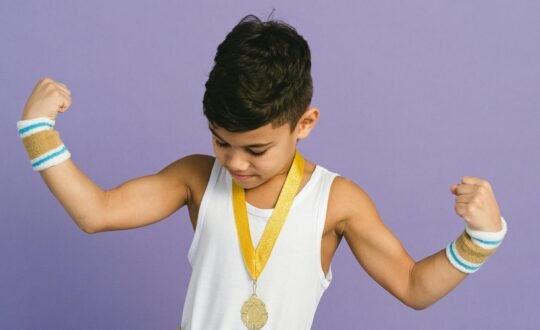 Young boy flexing muscles wearing a medal against a purple background.